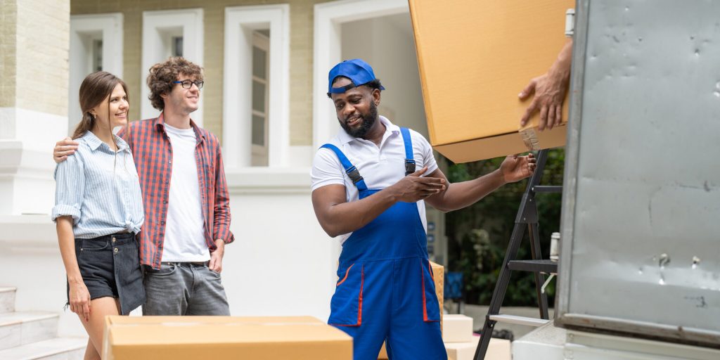 Man movers worker in blue uniform unloading cardboard boxes from truck.Professional delivery and moving service.